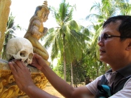 Sak handles one of the skulls exposed in the memorial's second tier encasement - Wat Samdech Mony, Battambang